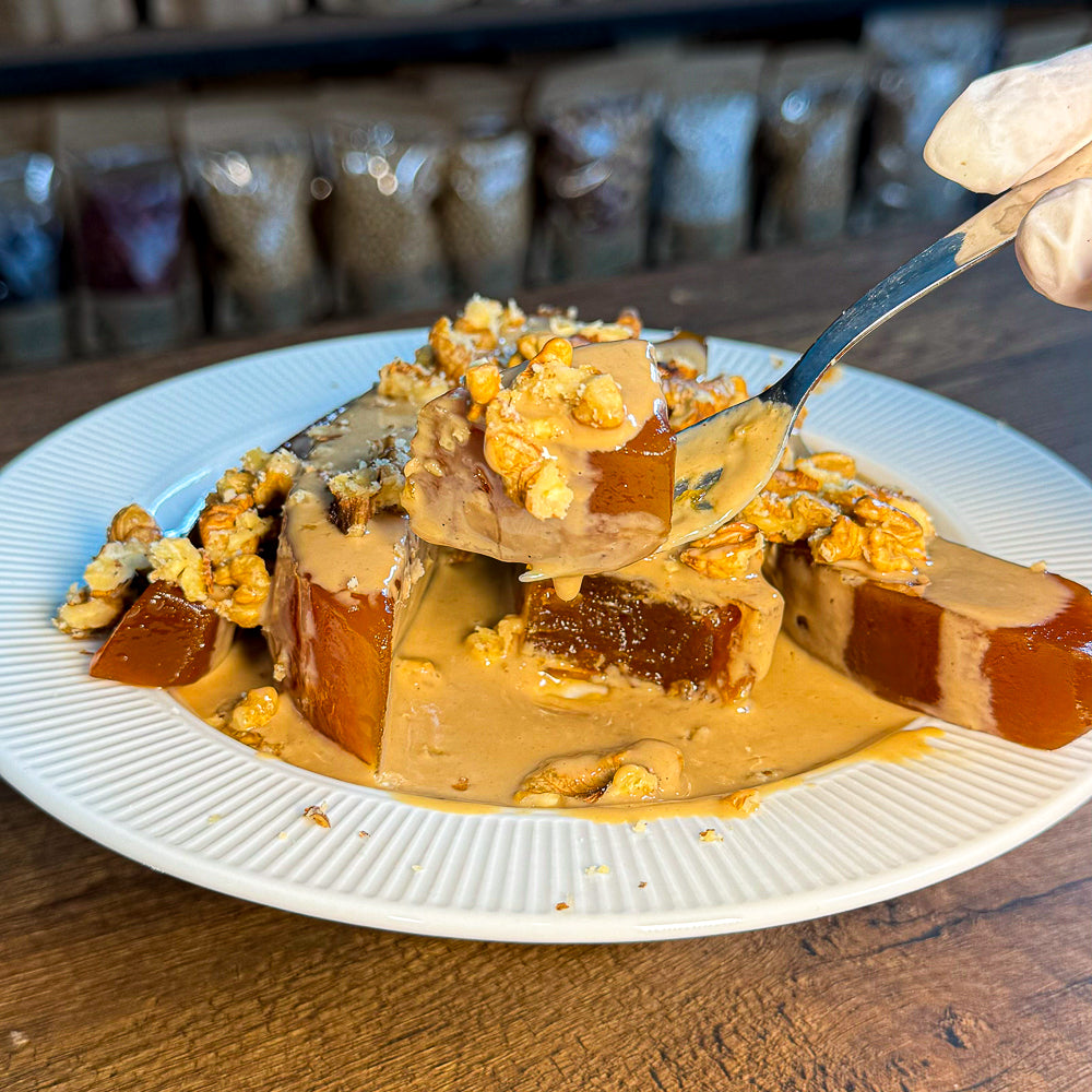 Klasik beyaz tabakta tahin soslu, ceviz parçalarıyla süslenmiş geleneksel balkabağı tatlısı.