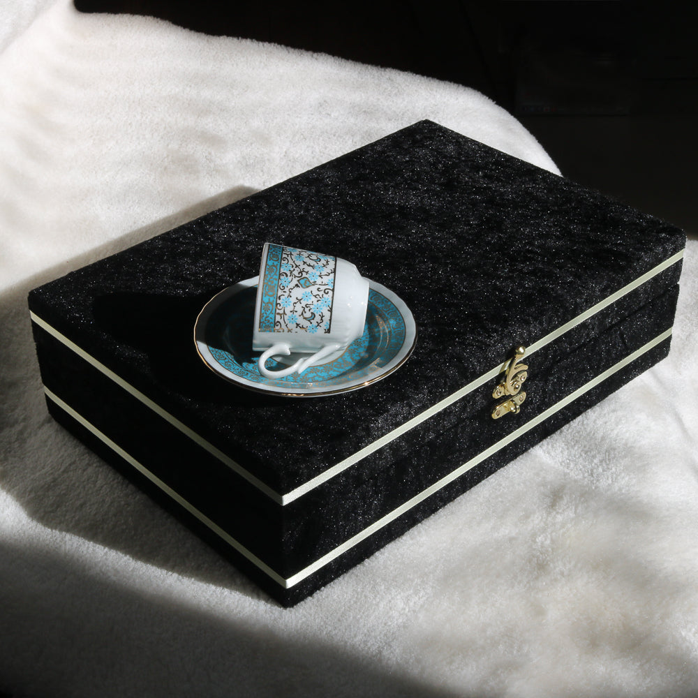 Siyah kadife kutu üzerinde altın detaylı, mavi desenli porselen fincan ve tabağı.